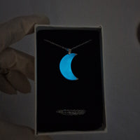 Necklace with a blue pendant in a box held by a hand against a dark background